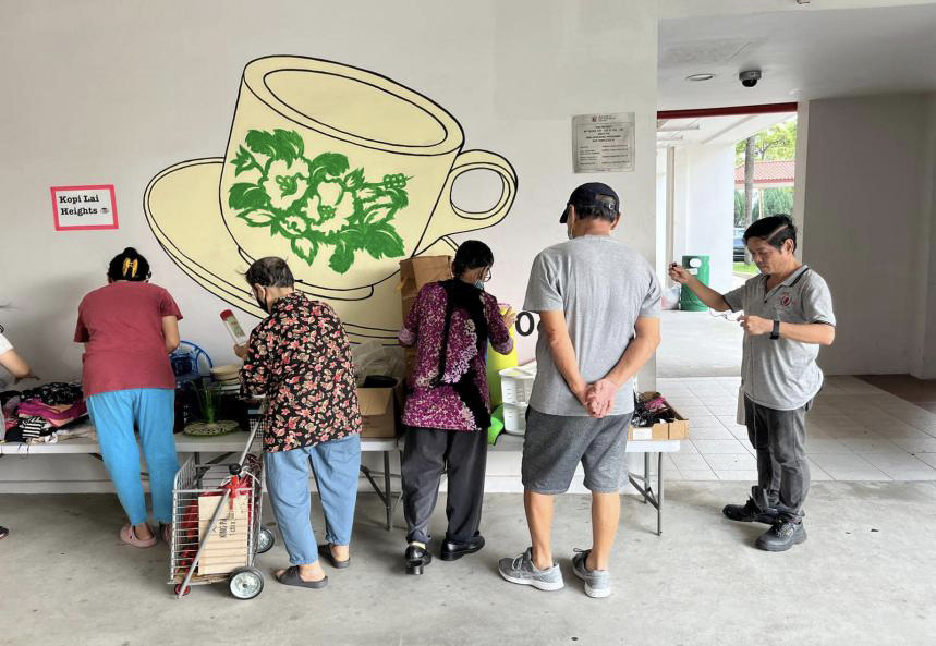 People gathered round a stall beside a poster showing a large teacup and saucer